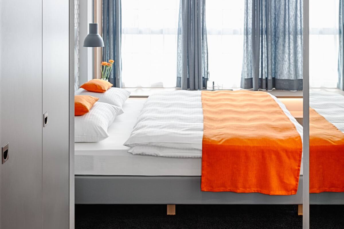 A modern hotel room with a bed, a nightstand, a lamp, and a view of the water.