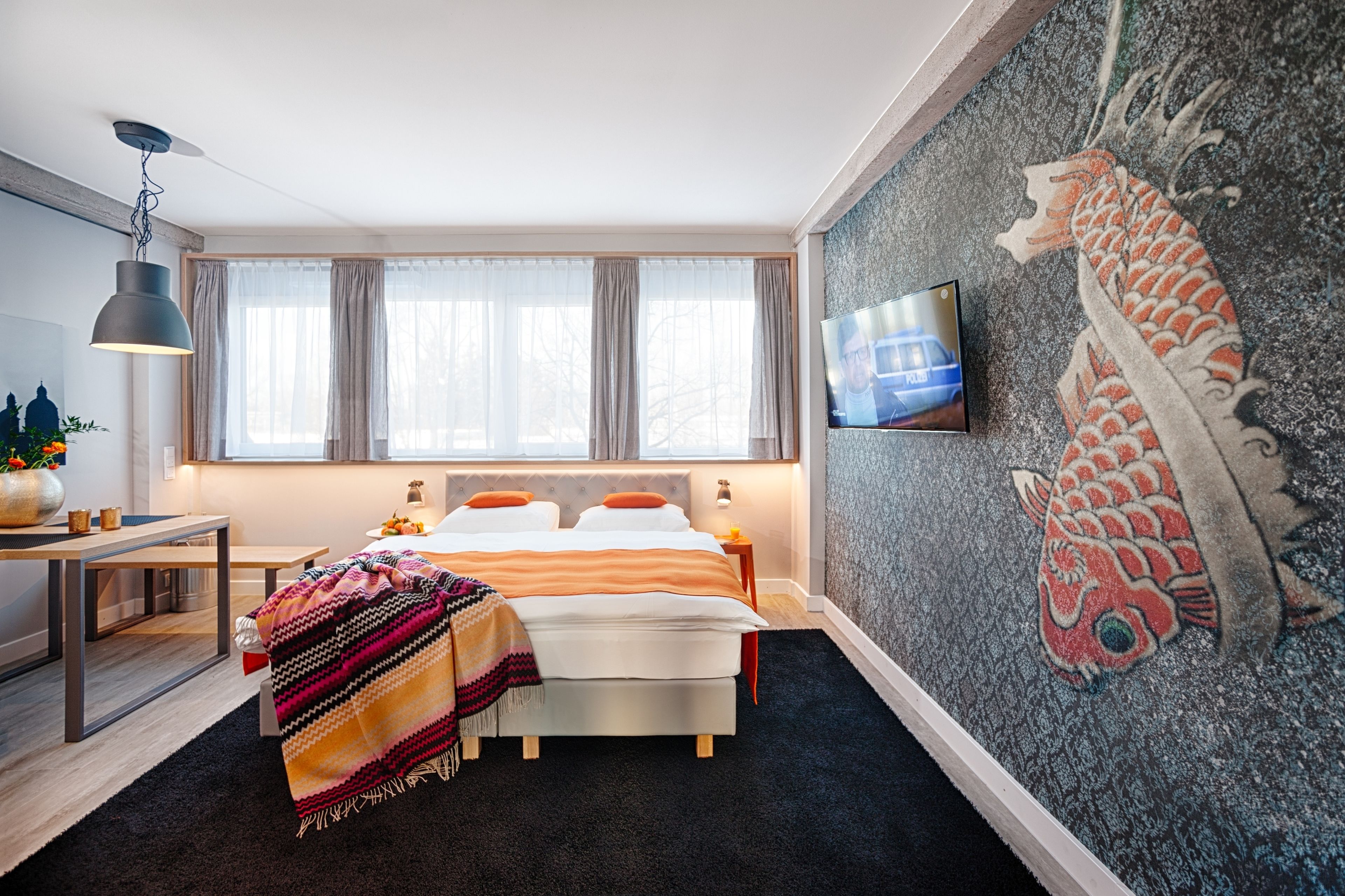 Un dormitorio moderno con cama, mesitas de noche, televisor y un mural decorativo en la pared.