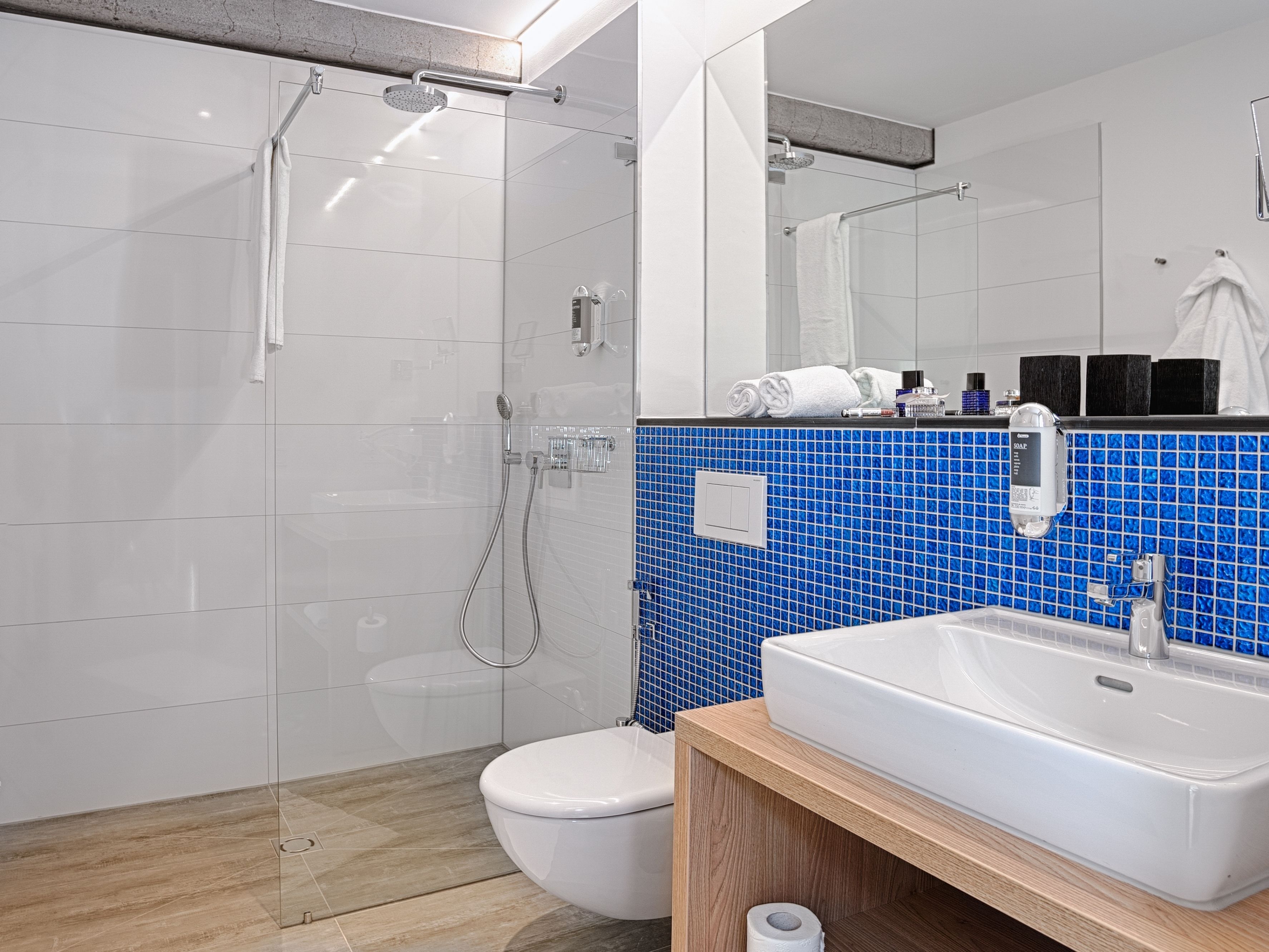 A modern bathroom with a glass shower enclosure, a white toilet, a sink with a soap dispenser, and a mirror above the sink.
