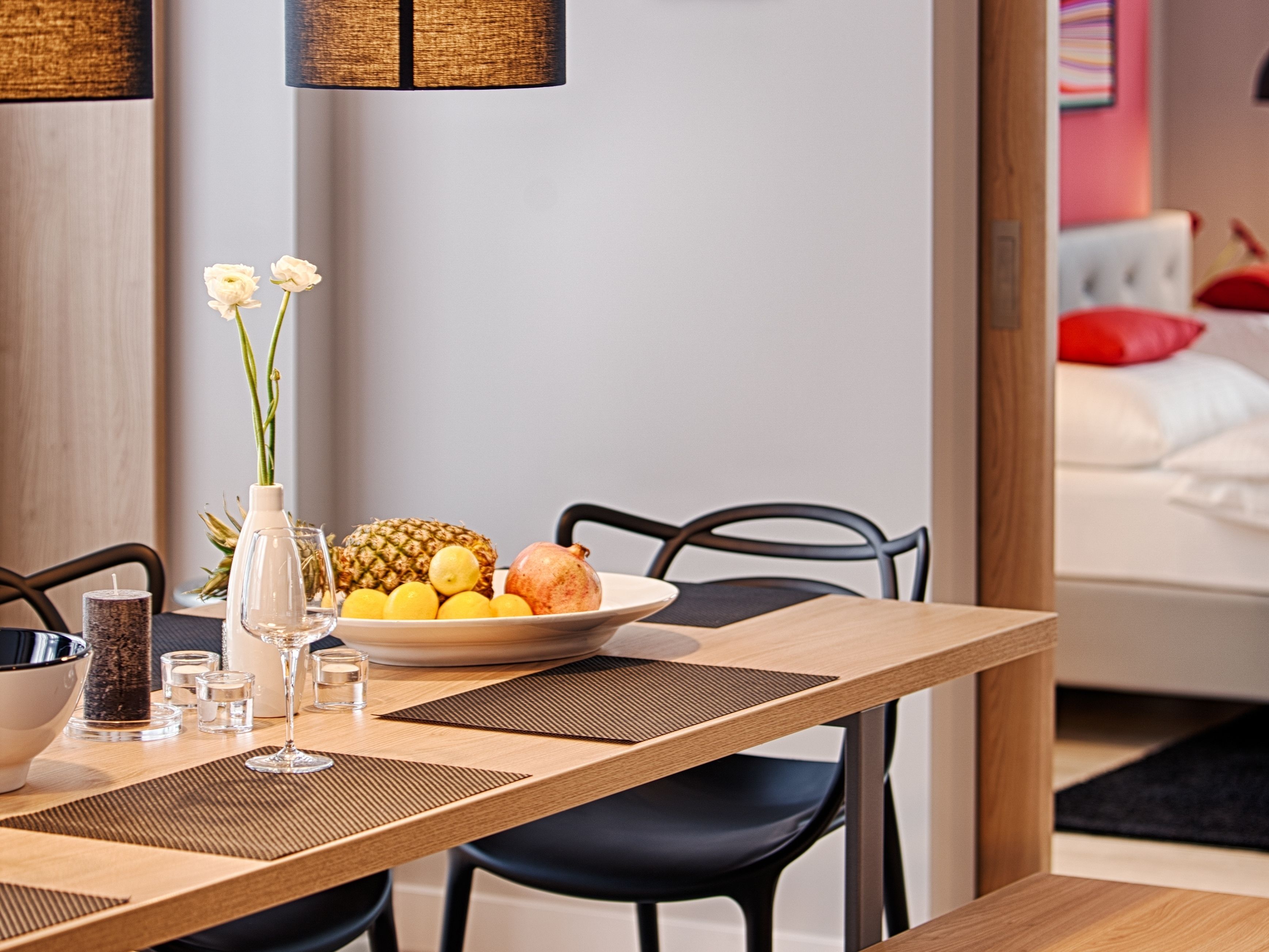 A dining table with a fruit bowl, a vase with flowers, and a candle.