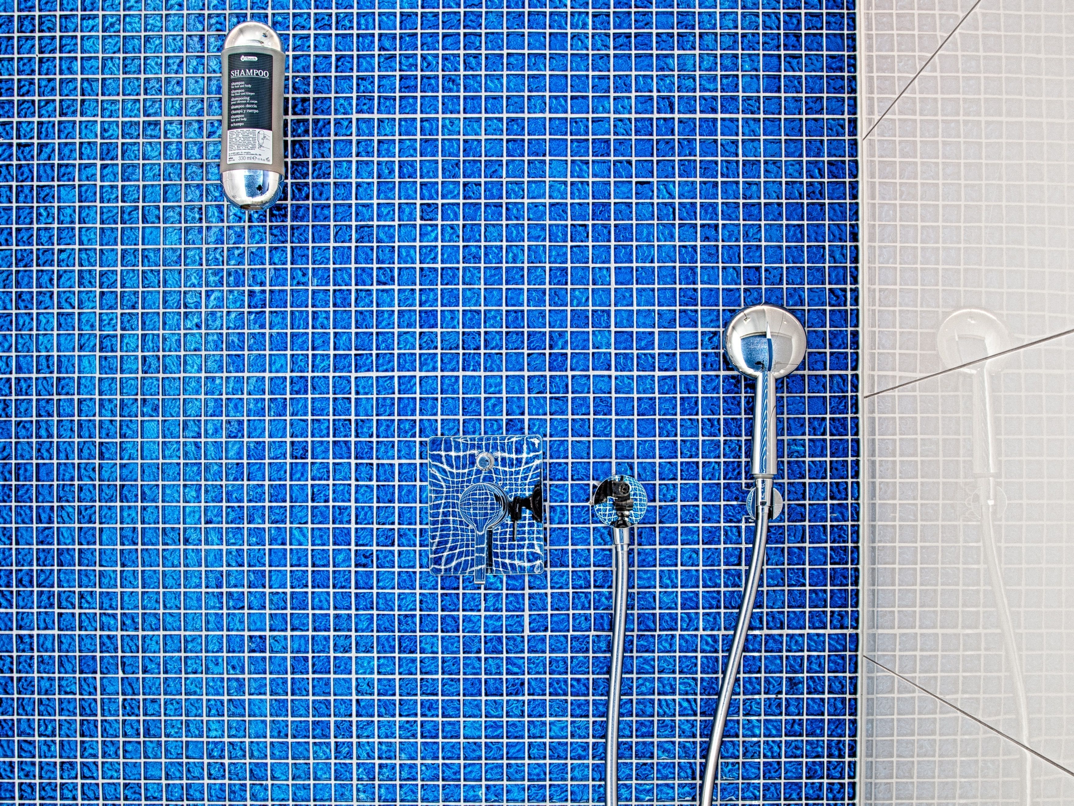 A bathroom with a blue tiled floor, a showerhead, and a handheld shower attachment.