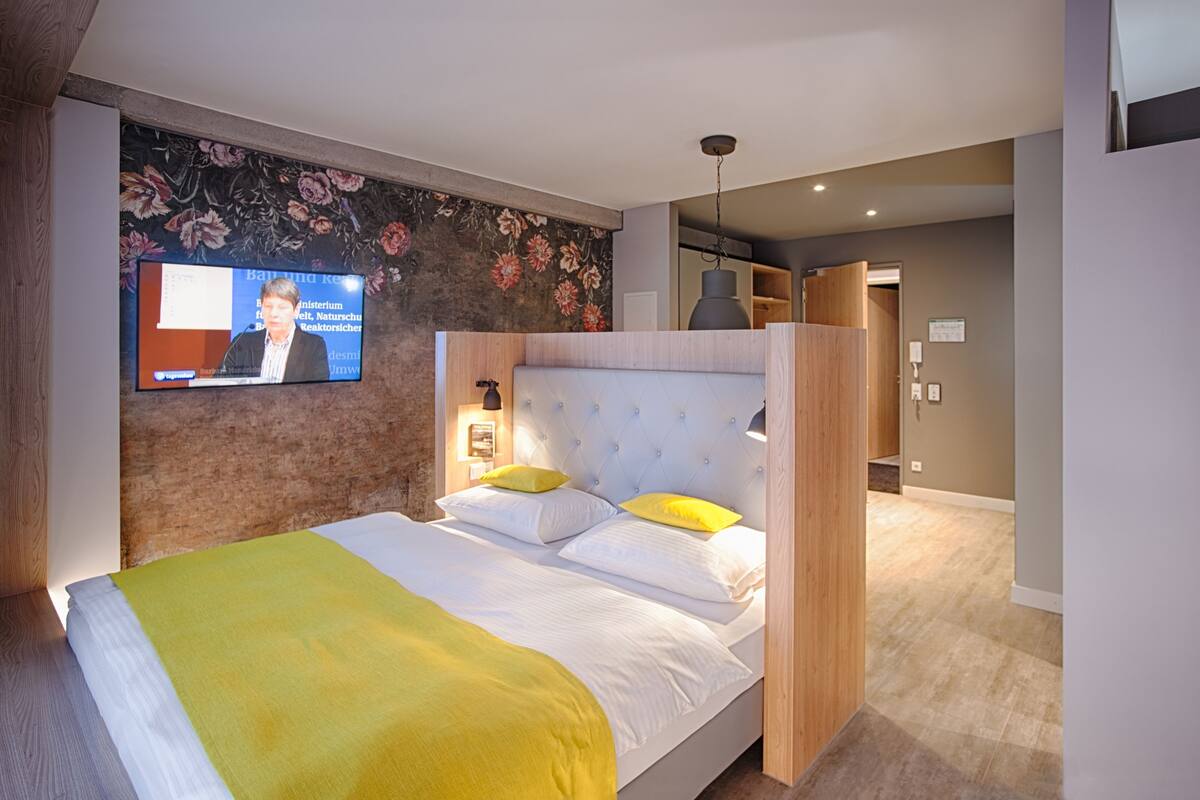 A hotel room with a large bed, a television on the wall, and a wooden headboard.