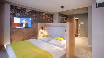 A hotel room with a large bed, a television on the wall, and a wooden headboard.