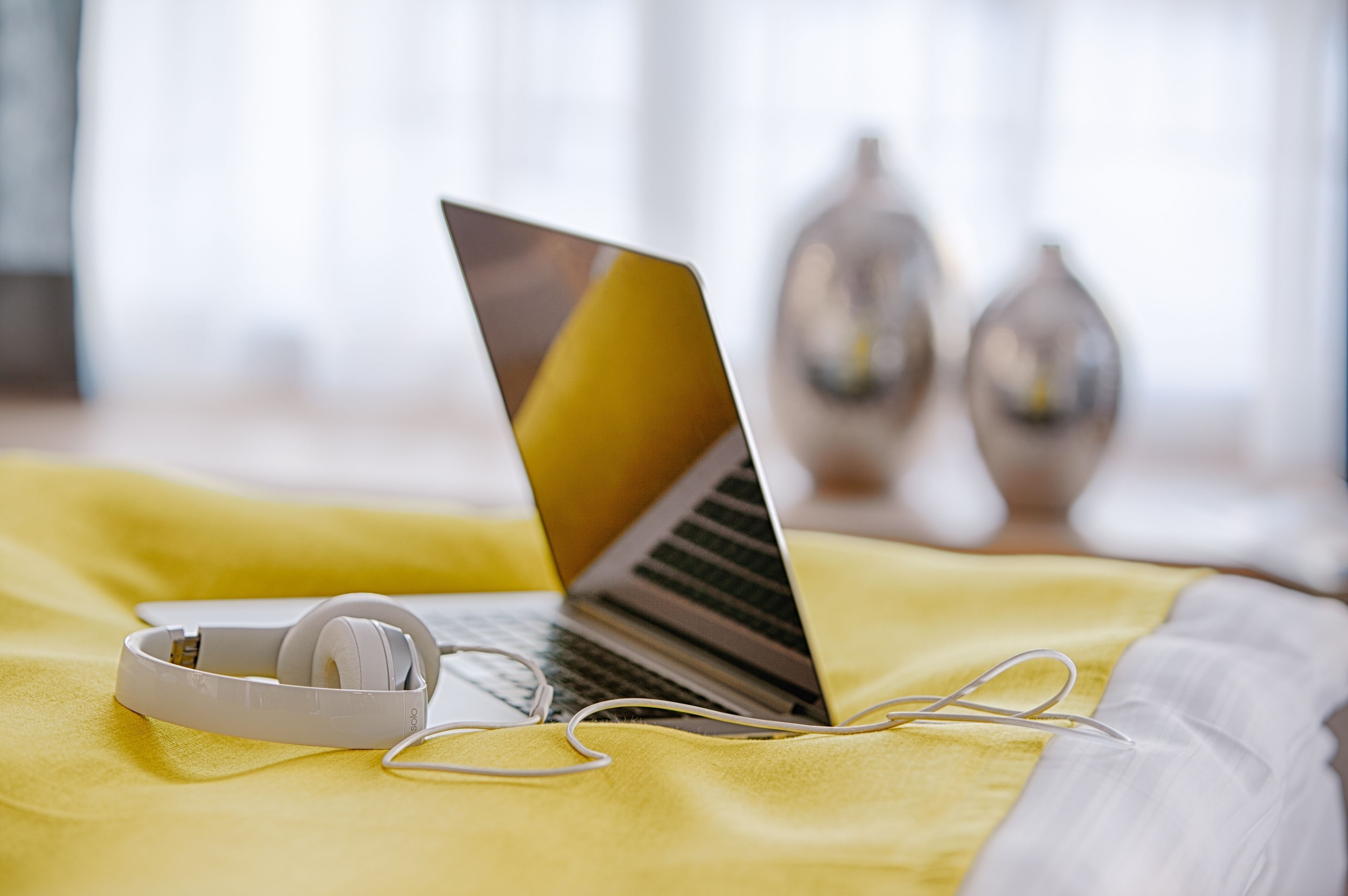 Una laptop sobre una manta amarilla, con auriculares y una almohada blanca.