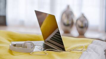 Una laptop sobre una manta amarilla, con auriculares y una almohada blanca.
