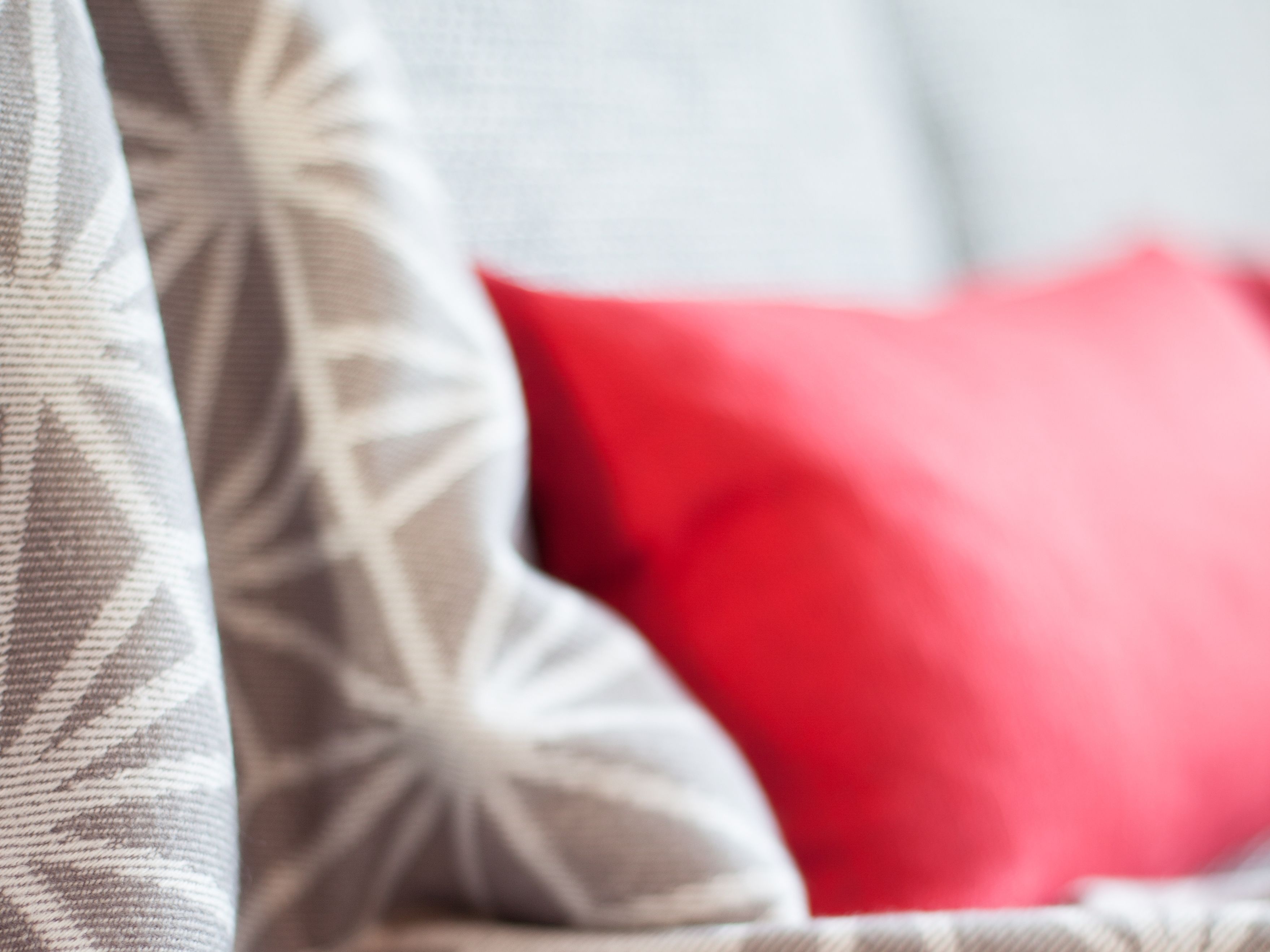 Een close-up van een gestreept patroon, waarschijnlijk onderdeel van een bank of sprei, met een rood kussen op de achtergrond.