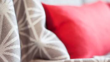 Een close-up van een gestreept patroon, waarschijnlijk onderdeel van een bank of sprei, met een rood kussen op de achtergrond.