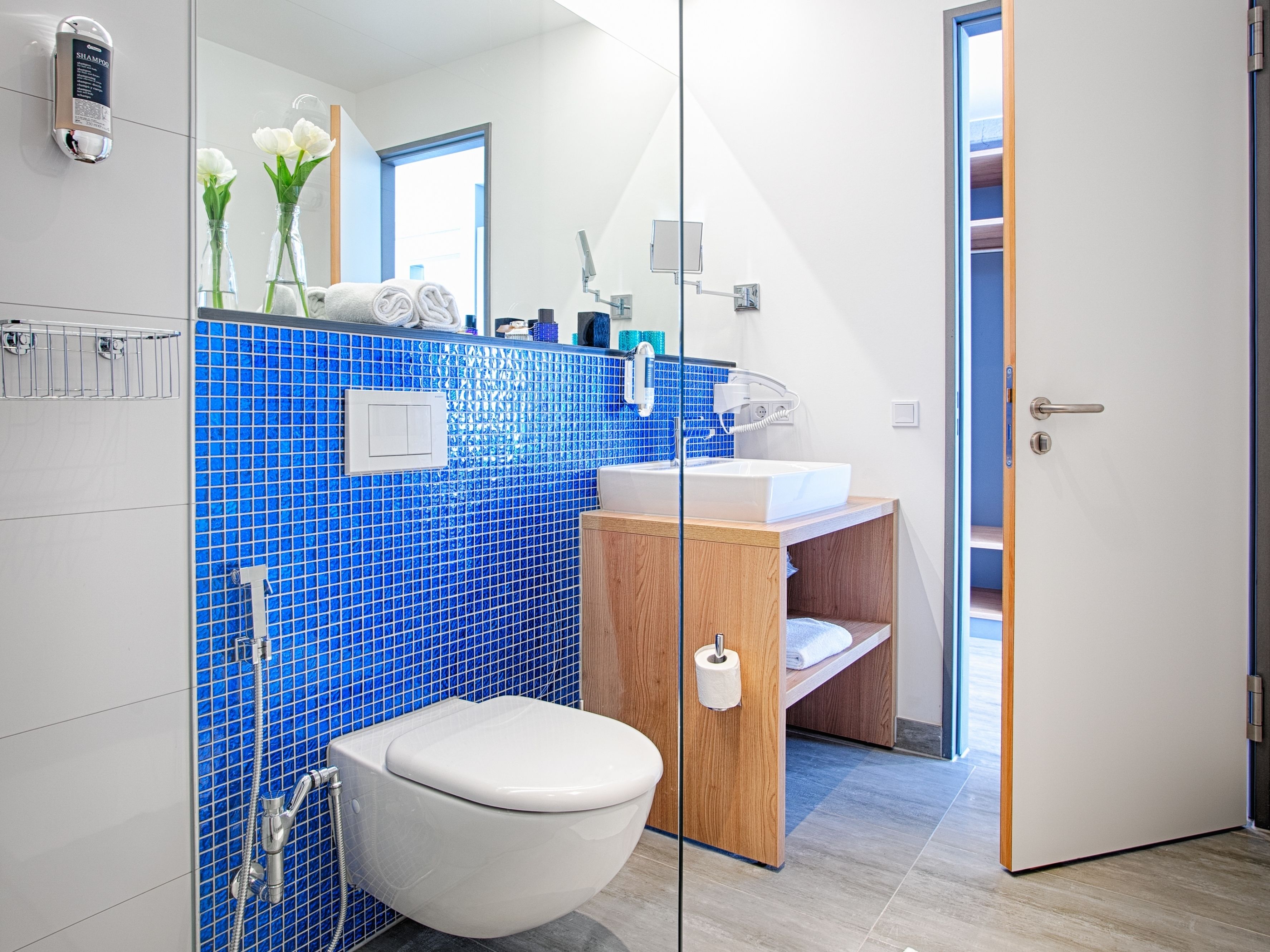 A modern bathroom with a white toilet, a wooden vanity, a sink, and a shower.