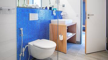 A modern bathroom with a white toilet, a wooden vanity, a sink, and a shower.