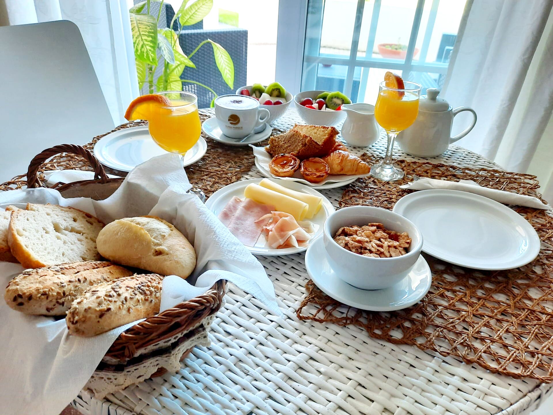 Una mesa de desayuno con pan, pasteles, frutas y bebidas.