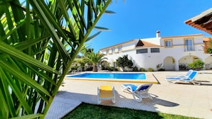 A swimming pool with lounge chairs, a white building with arches, and a clear blue sky.