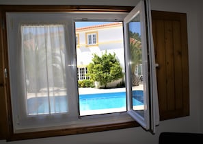 A room with a window overlooking a swimming pool and a building with yellow trim.