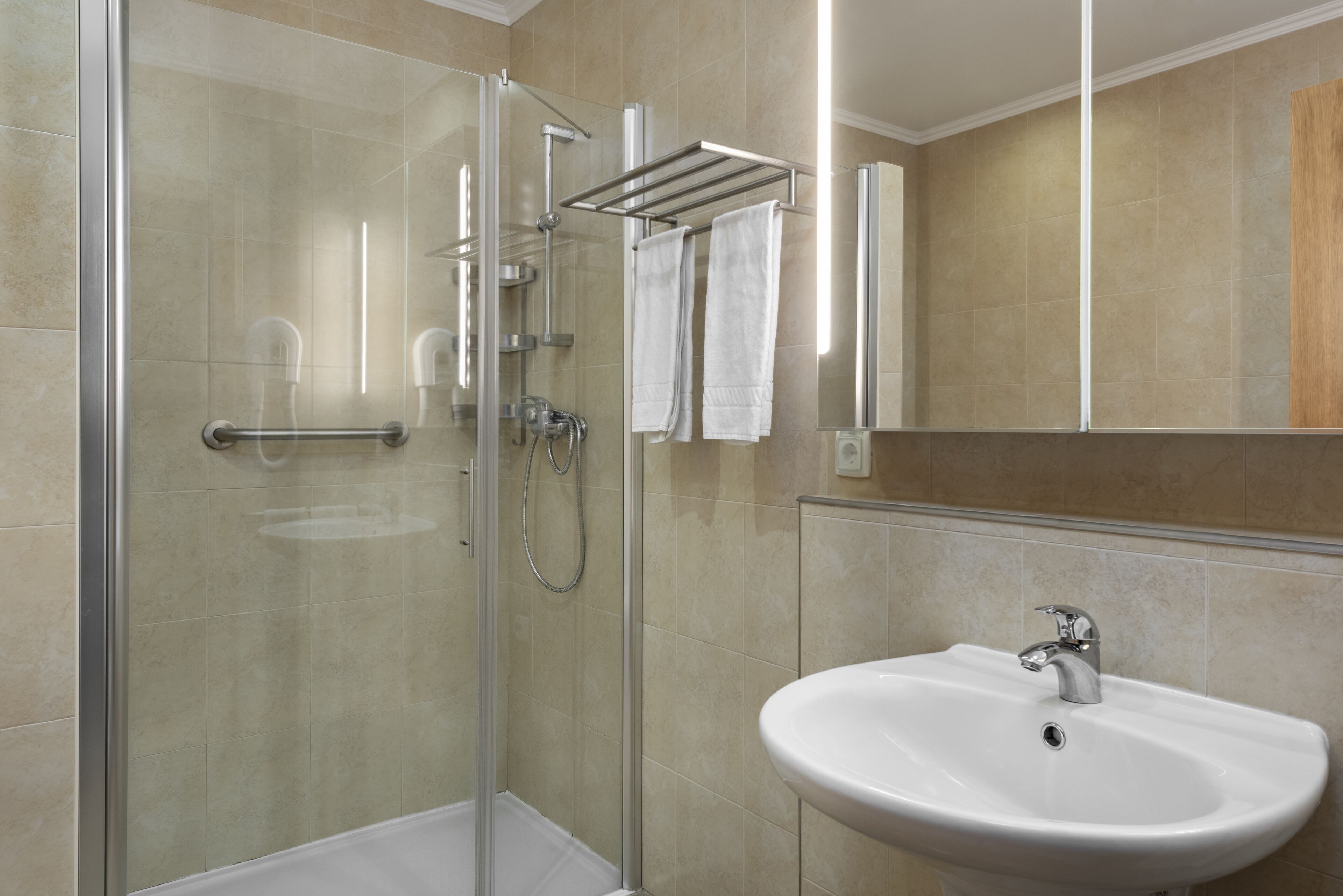 A modern bathroom with a glass-enclosed shower, a white sink, and a towel rack.