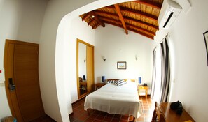 Une chambre à coucher avec un lit, une porte en bois, un miroir, un tableau accroché au mur et une fenêtre avec des rideaux.