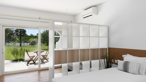 A modern bedroom with a large bed, a sliding glass door leading to an outdoor patio, and a view of a garden.
