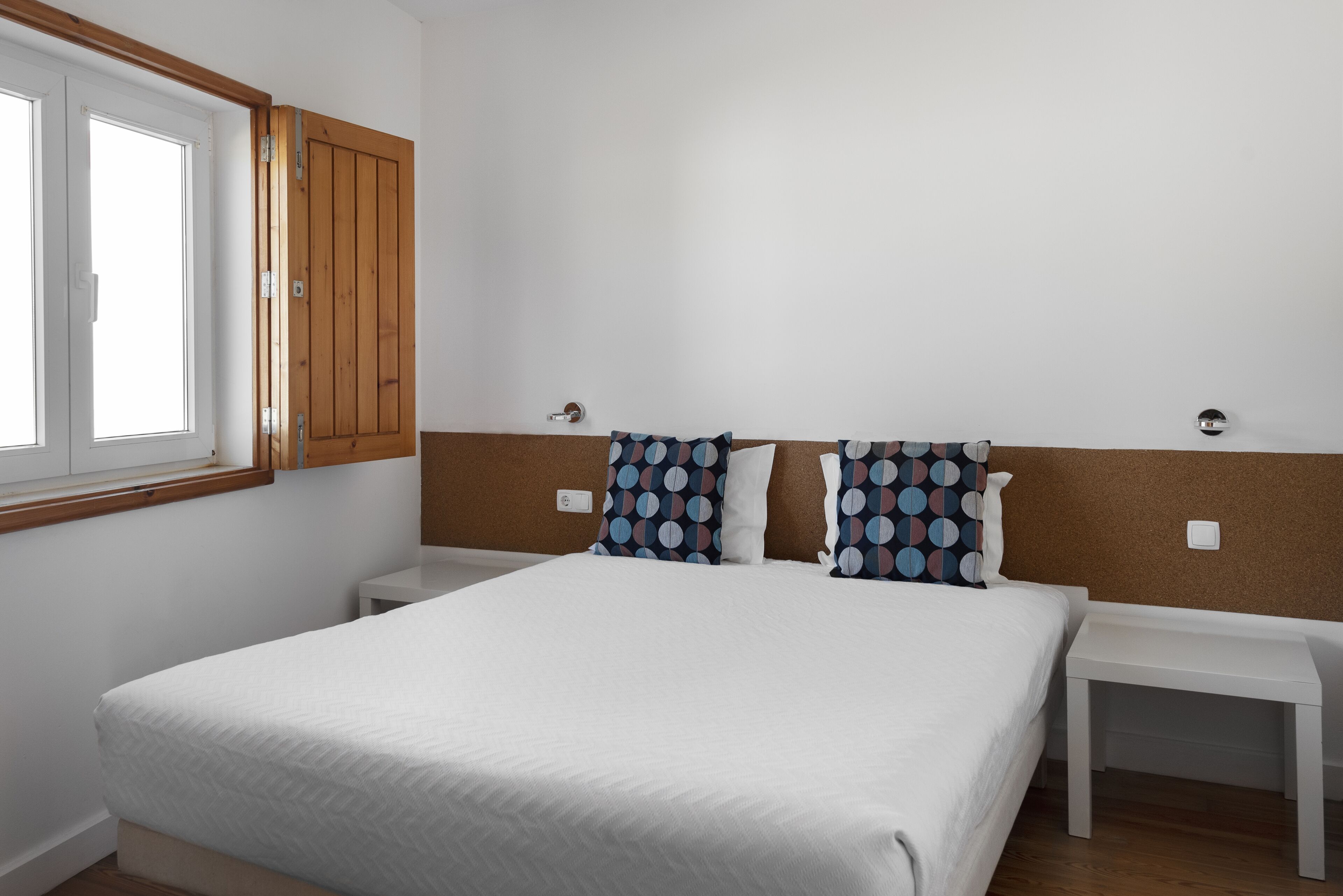 A bedroom with a large bed, two bedside tables, a window, and a wooden wardrobe.