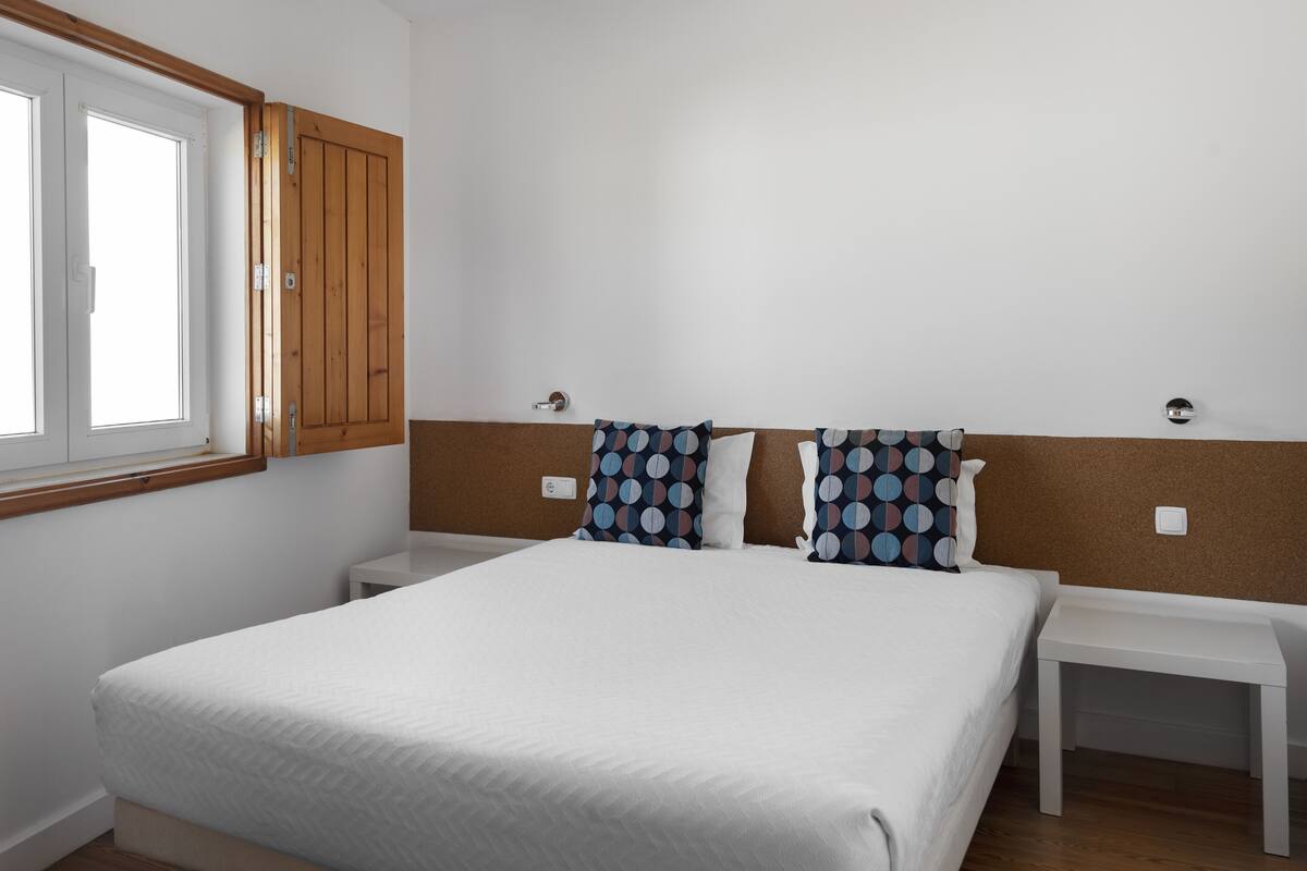 A bedroom with a large bed, two bedside tables, a window, and a wooden wardrobe.