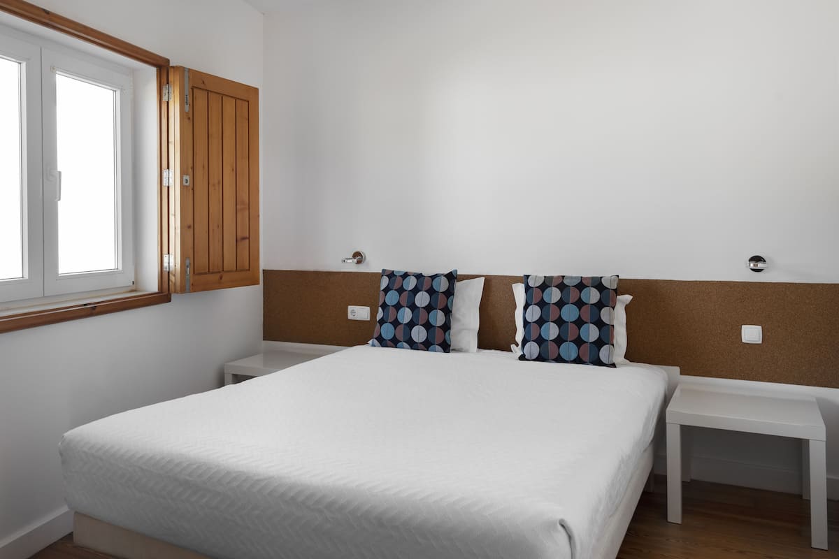 A bedroom with a large bed, two bedside tables, a window, and a wooden wardrobe.