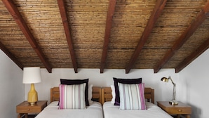 A room with two beds, wooden headboards, a wooden ceiling, a nightstand with a lamp, and a bedside table with a lamp.