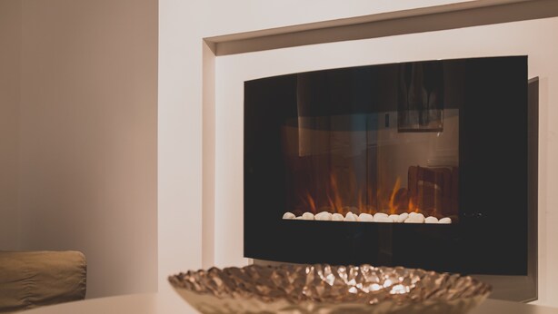 En modern öppen spis med en böjd design, en dekorativ skål framför och en vägg i en neutral färg.