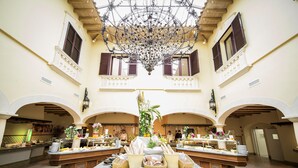 Um átrio amplo com uma fonte central, diversas mesas de buffet e um imponente candelabro.