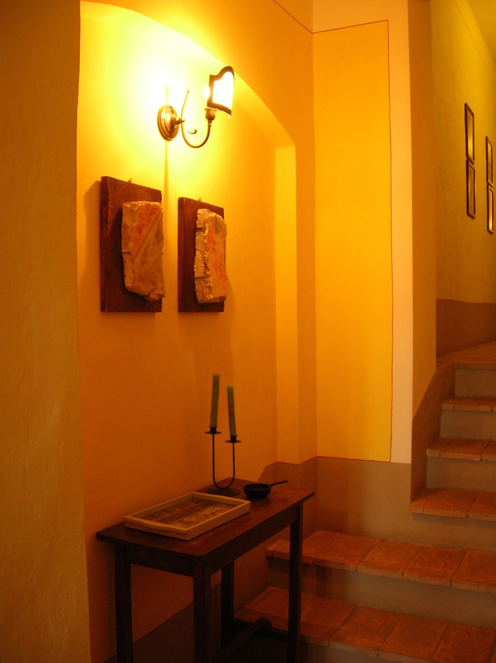 Un pasillo cálidamente iluminado con una mesa de madera, dos toallas colgadas en la pared y una escalera.