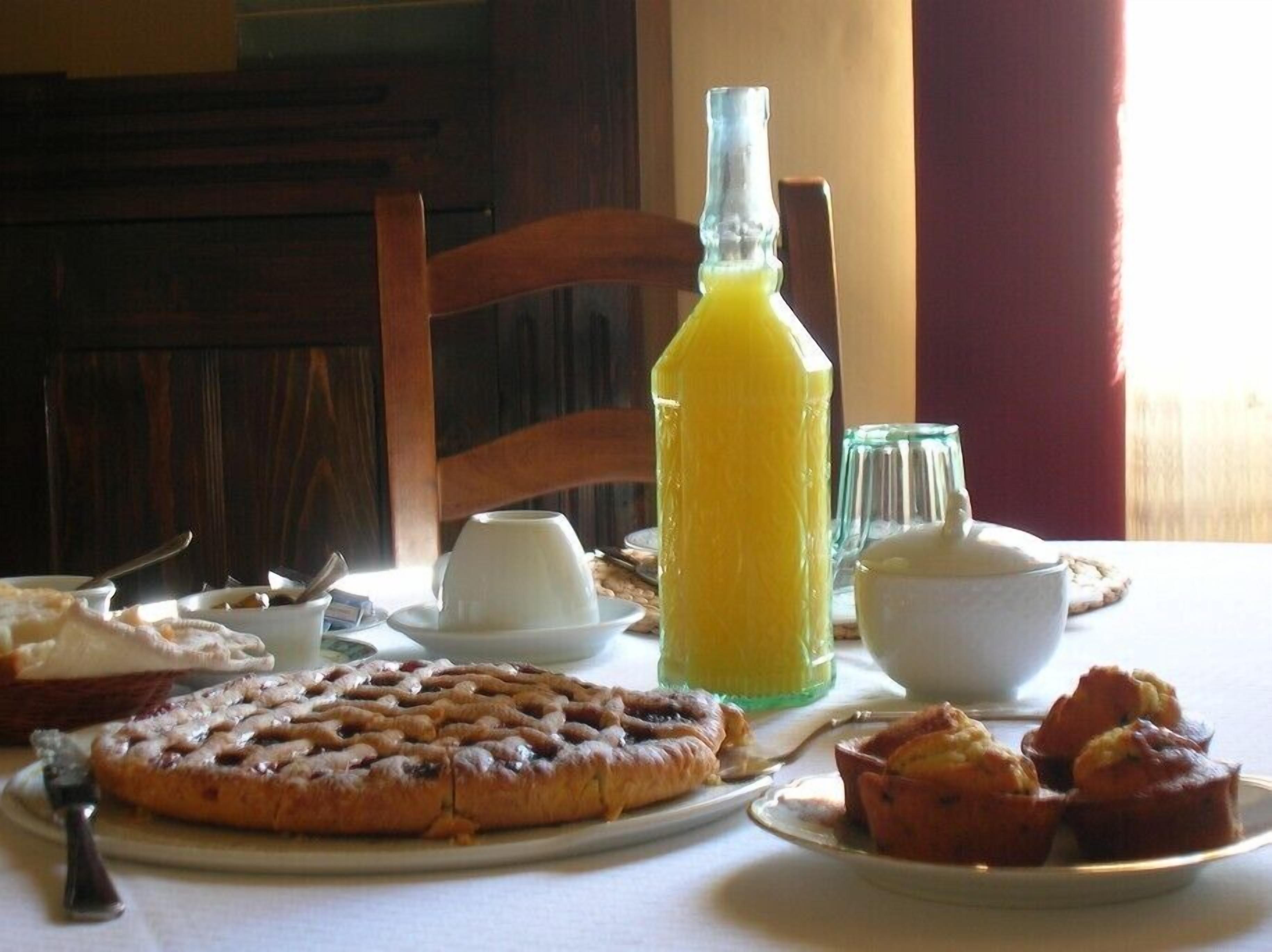 A breakfast table with a fruit tart, muffins, and a bottle of orange juice.