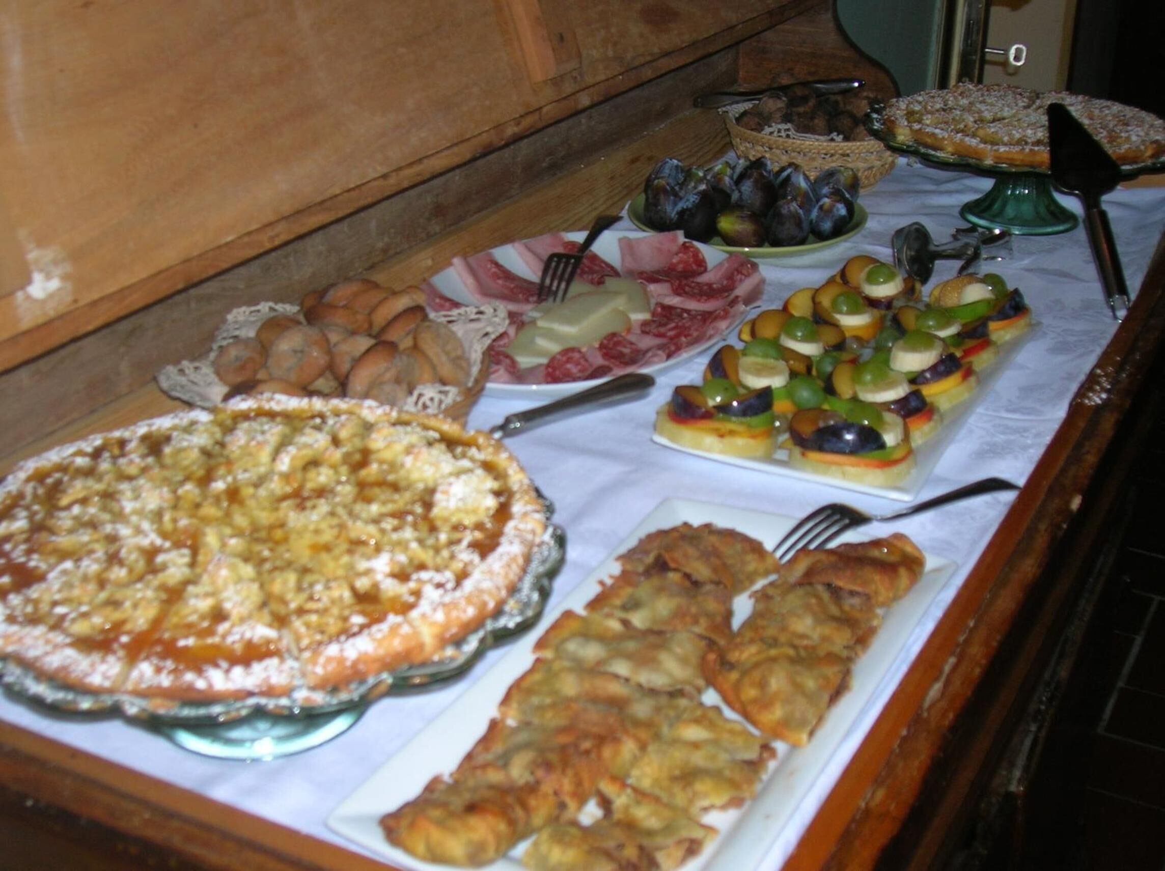 Una mesa de buffet con diversos platos, incluyendo una tarta grande, fuentes de fruta y otros alimentos.
