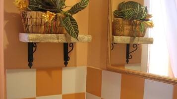A bathroom with orange and white checkered tiles, a white bathtub, two wall-mounted shelves with potted plants, and a mirror with a gold frame.