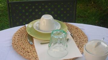 A table set outdoors with a woven placemat, a white cup and saucer, a glass pitcher, and a bowl of almonds.