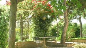 Un patio con una mesa y sillas de piedra, rodeado de árboles y un muro de ladrillo.
