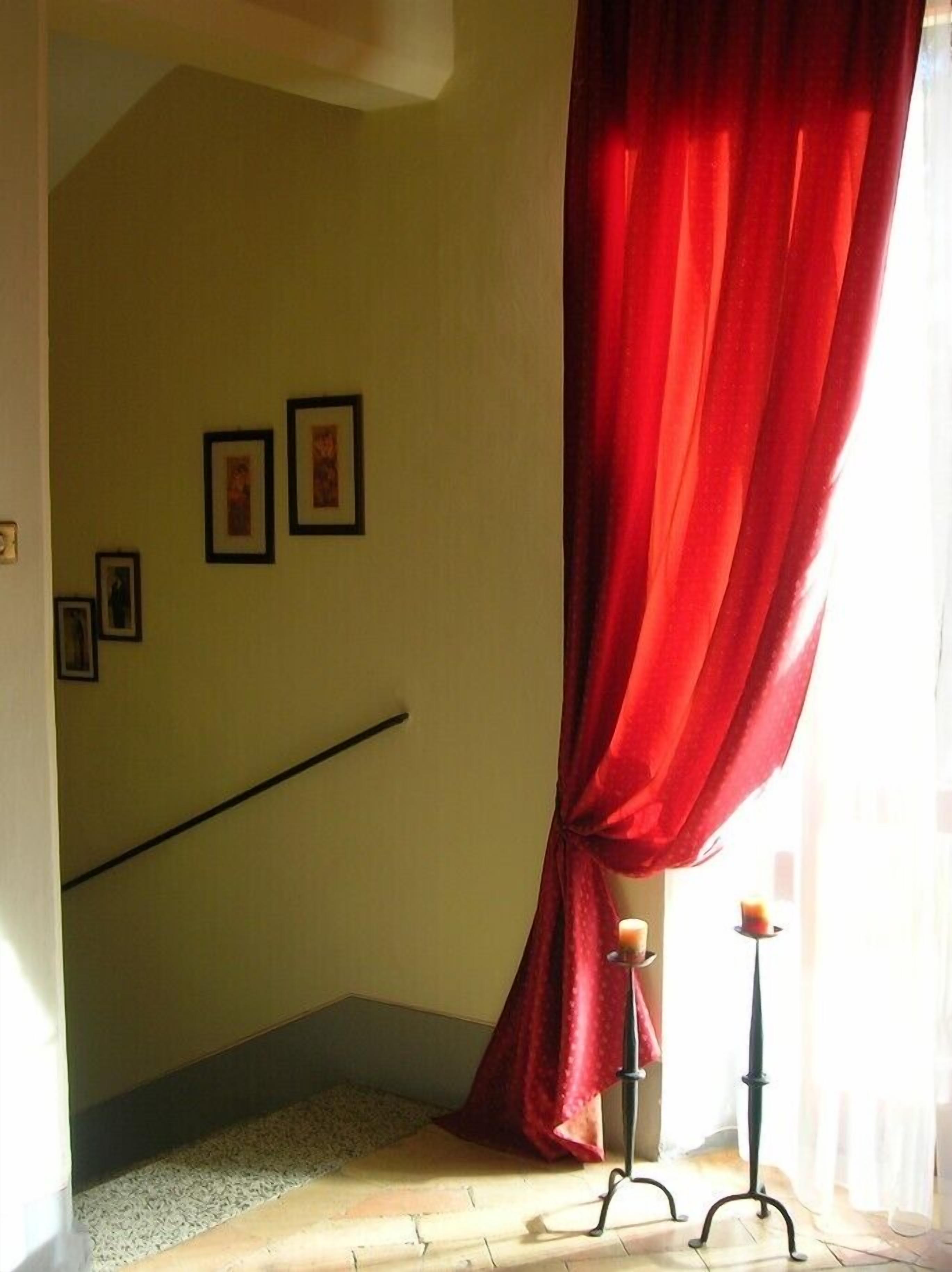 Una habitación con una escalera, una cortina roja y un candelabro.