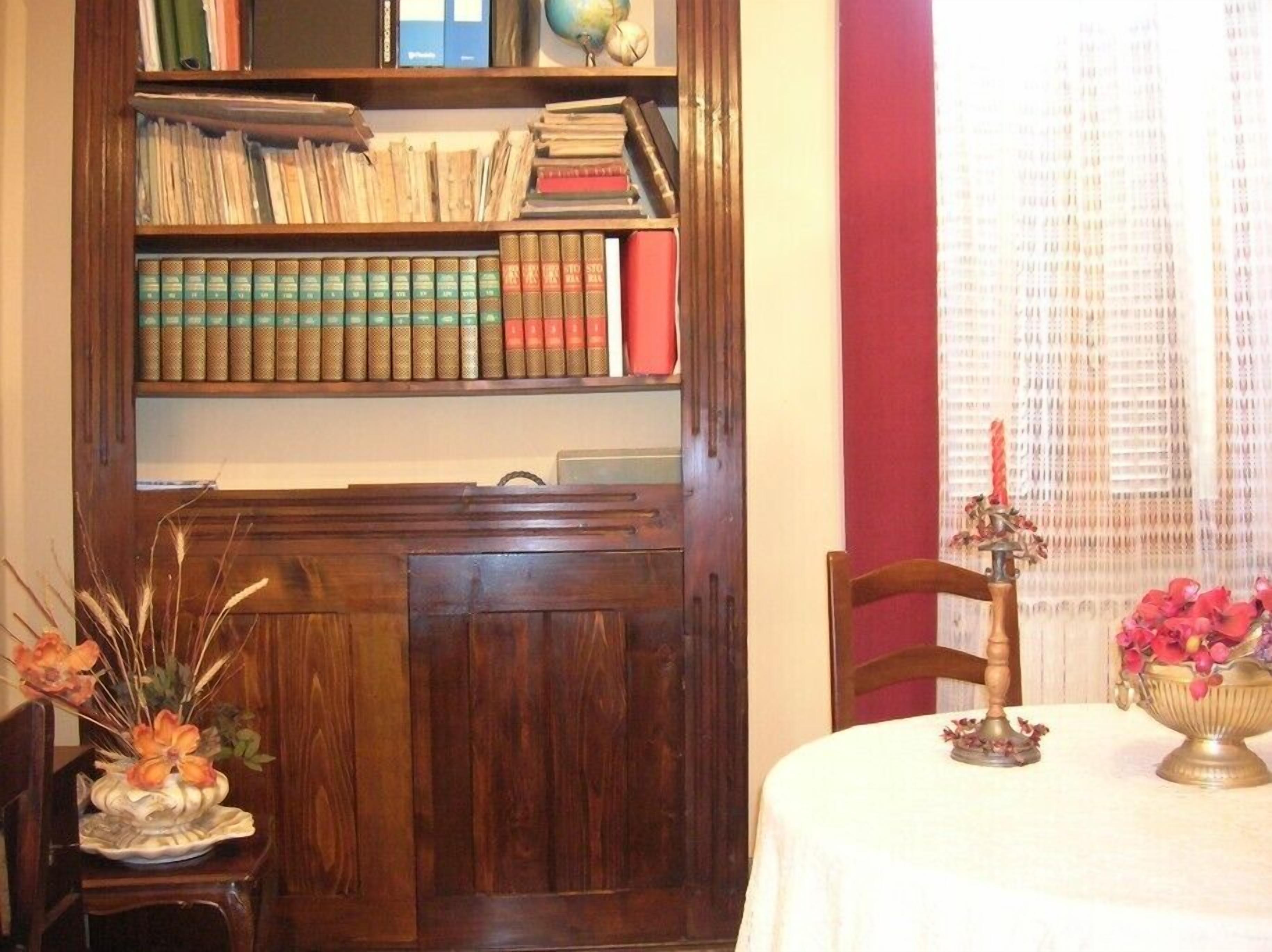 A wooden bookshelf filled with books, a globe, and a decorative vase with flowers.
