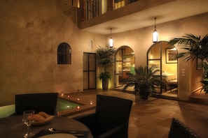 Un patio interior acogedor con piscina, mobiliario de mimbre e iluminación ambiental.