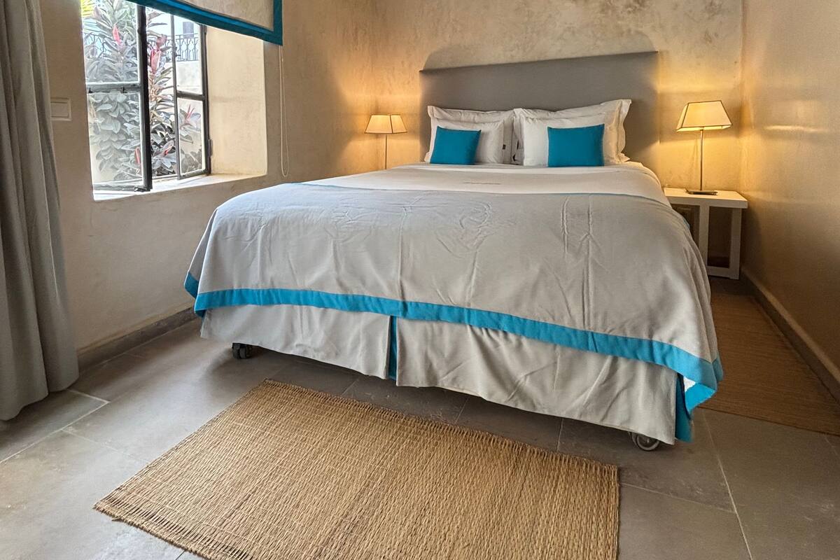 A bedroom with a bed, two bedside tables with lamps, a window with curtains, and a textured rug.