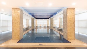 Una piscina interior moderna con paredes de vidrio transparente, suelo de azulejos azules y techo revestido de azulejos.