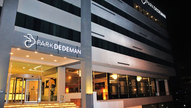 Un edificio moderno con un letrero que dice 'Park DeDeMan', que presenta una puerta giratoria y ventanas amplias.