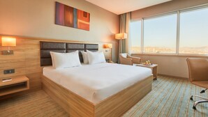 Una habitación de hotel con una cama grande, un escritorio, una silla y una ventana con vistas a la ciudad.