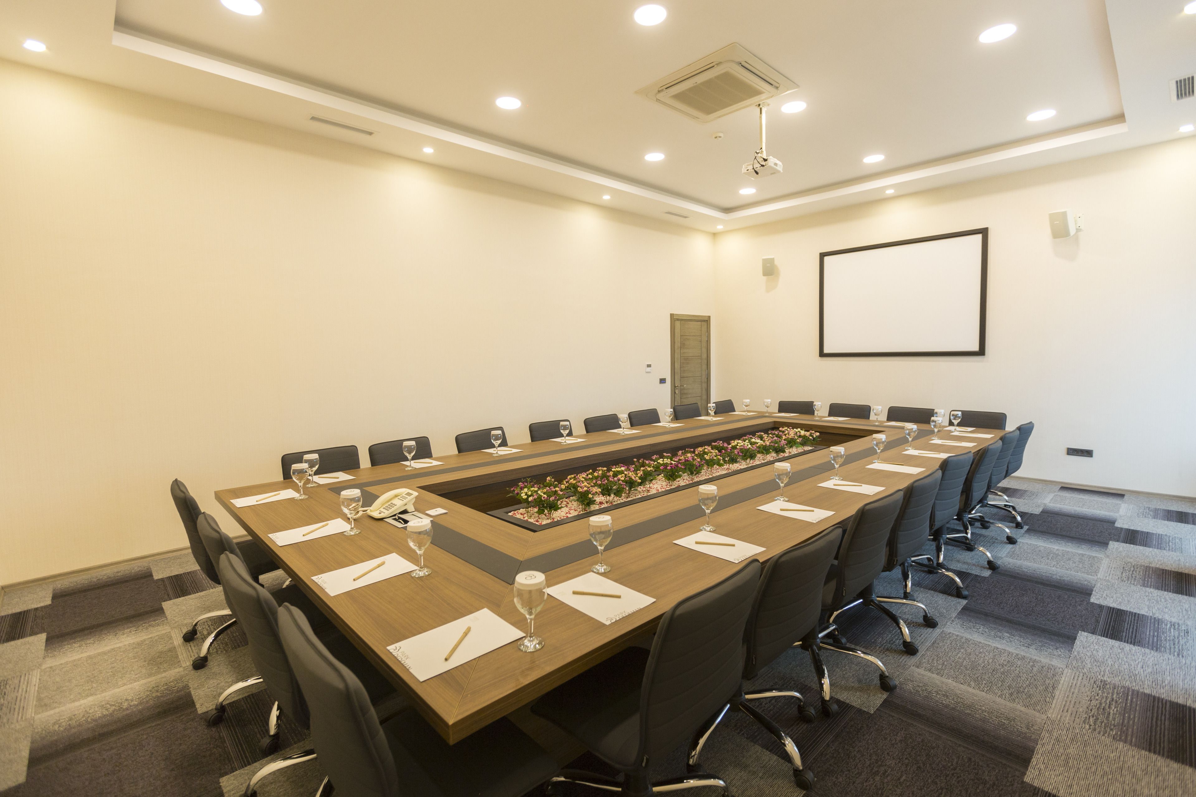 A conference room with a long table, chairs, and a projector screen on the wall.