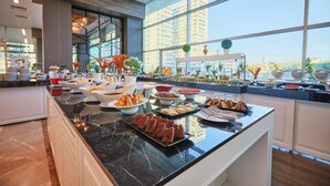 Un bufé con diversos alimentos y un amplio ventanal con vista a la ciudad.