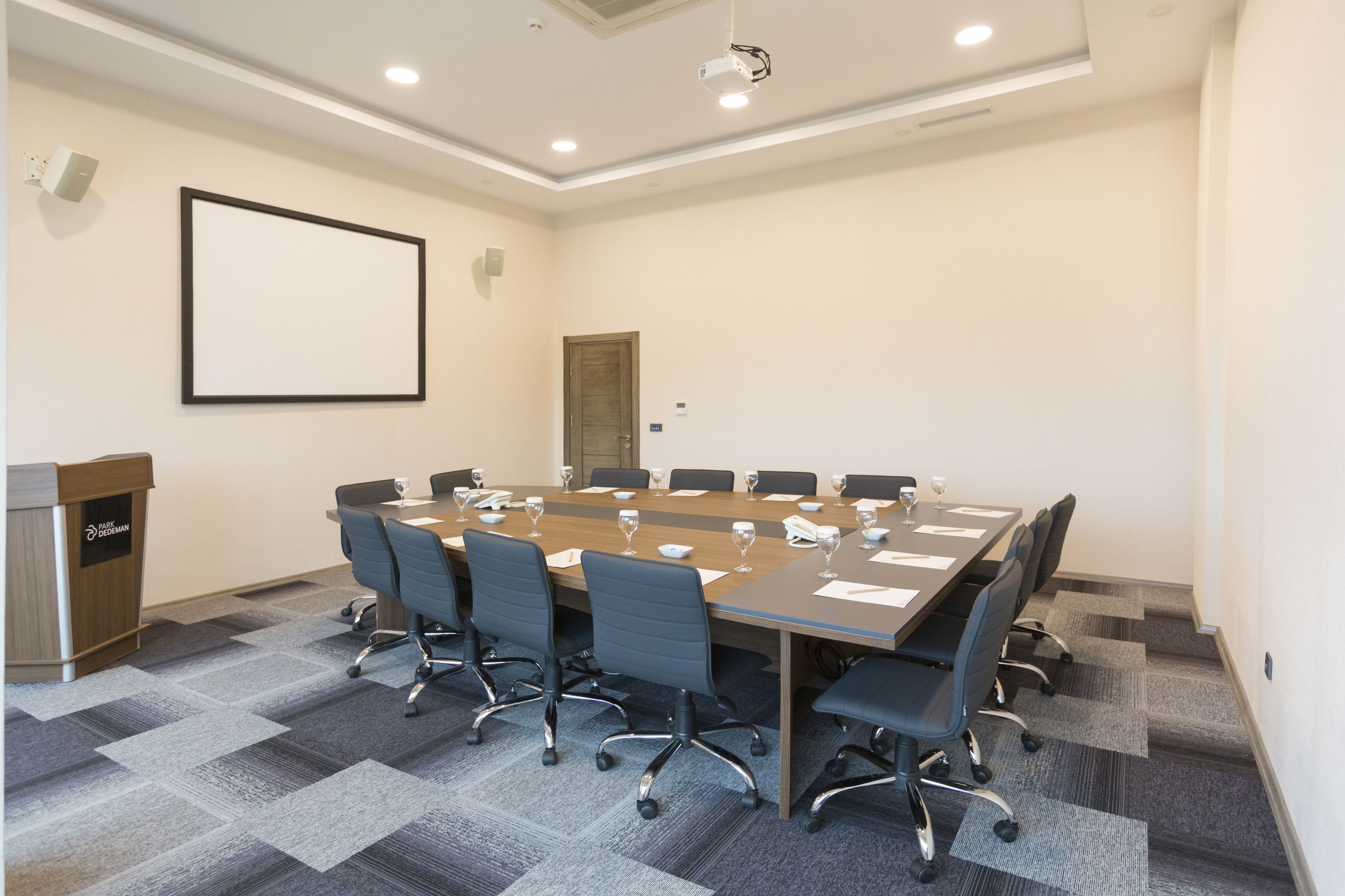 A conference room with a long table, chairs, a podium, and a projector screen.