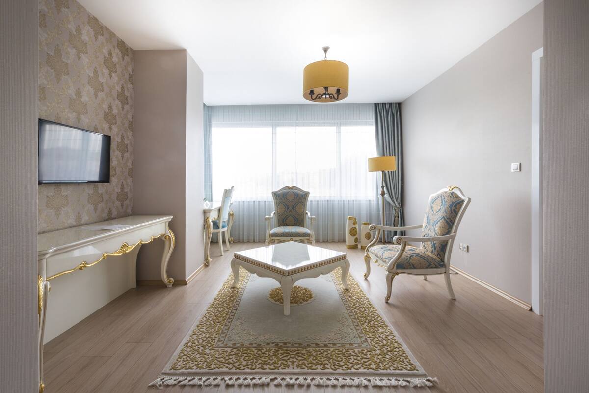 Una habitación de hotel moderna con un ventanal grande, un televisor de pantalla plana montado en la pared, una mesa de centro blanca y dos sillones estampados.