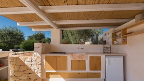 An outdoor kitchen with stone walls, wooden cabinets, and a built-in refrigerator. - Trullo Luna (Ostuni)