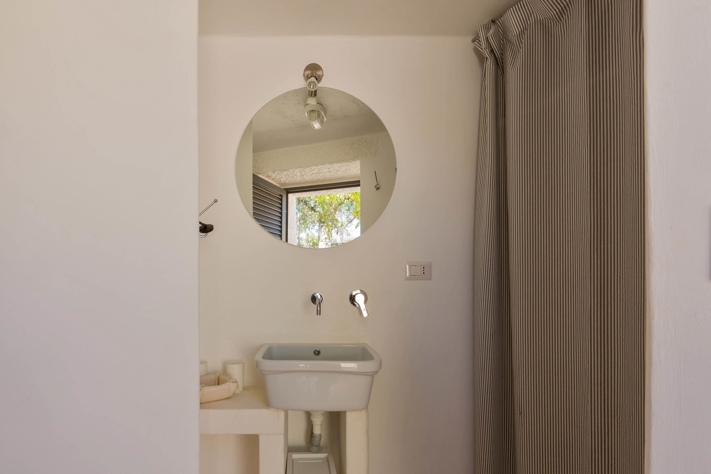 A bathroom with a round mirror, a white sink, and a striped shower curtain.