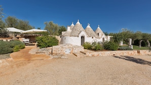 A white building with multiple conical roofs, a gravel driveway, and a stone pathway leading to a door. - Trullo Luna (Ostuni)
