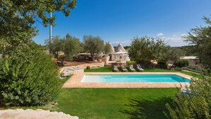 A swimming pool surrounded by a well-maintained lawn, a small gazebo, and a stone wall. - Trullo Luna (Ostuni)