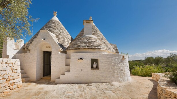 A traditional stone building with a central door and two conical roofs. - Trullo Luna (Ostuni)