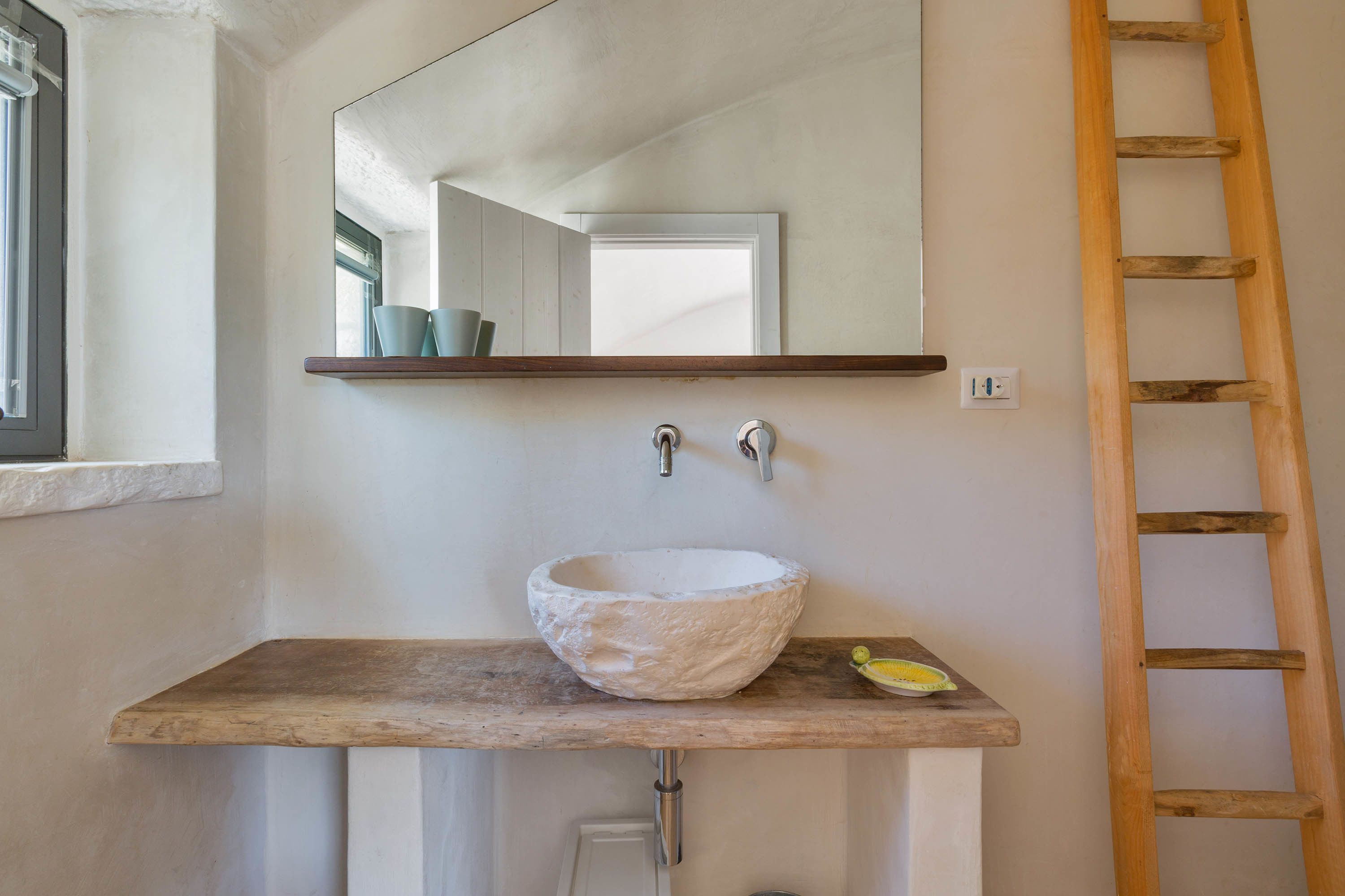 A bathroom with a wooden vanity, a white basin, a mirror, and a wooden ladder.
