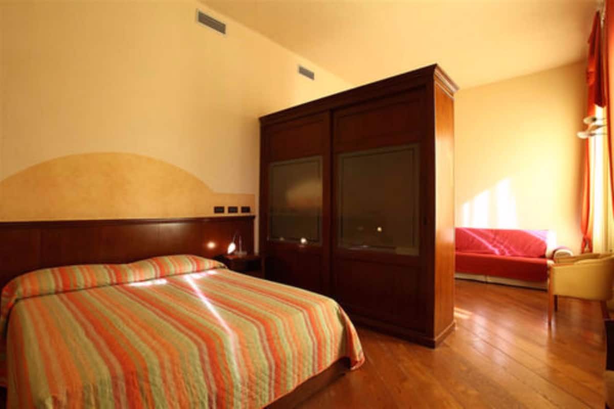 Una habitación de hotel con cama, armario, mesita de noche y ventana con cortinas.