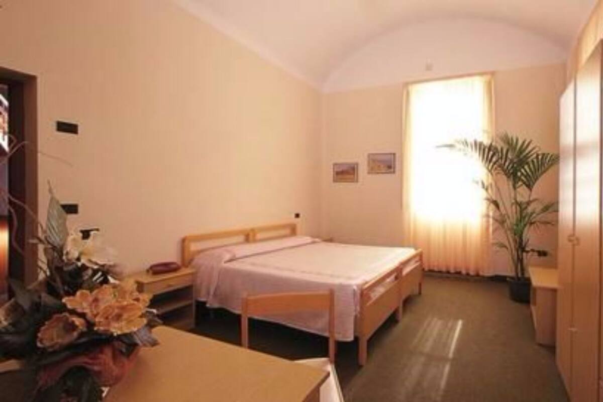 Habitación de hotel con una cama individual, un escritorio con silla, un armario y un ventanal con cortinas.
